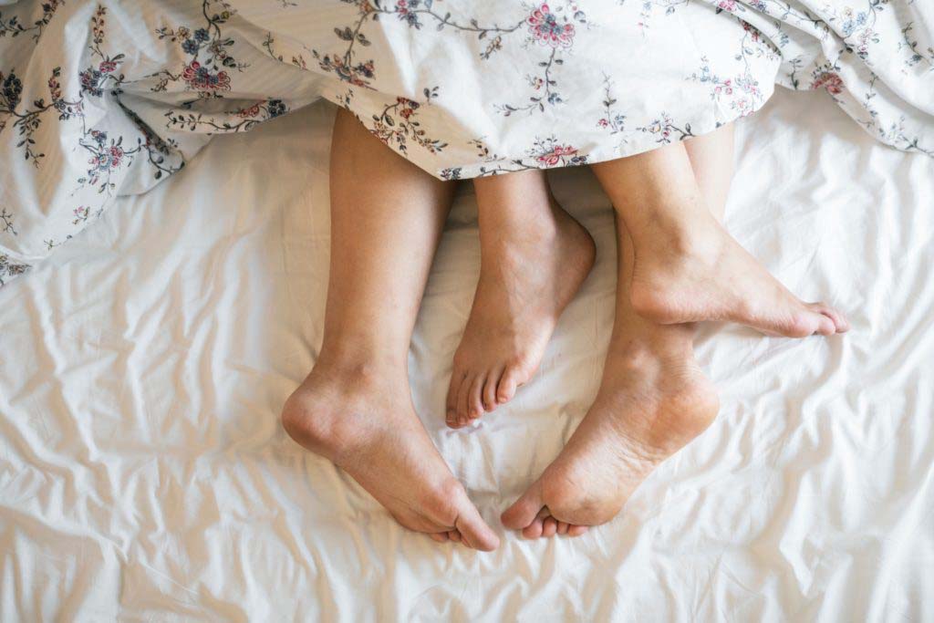 Two adults barefoot in bed (photo by rawpixel.com)